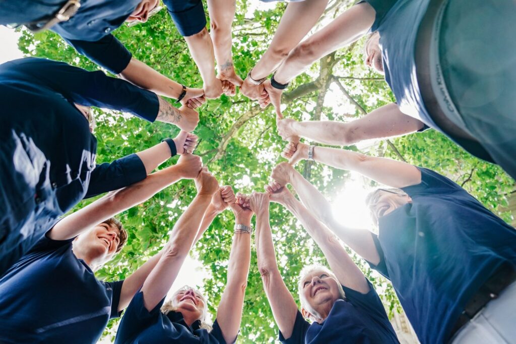 Das Team bildet mit den Fäusten einen Kreis unter einem Baum